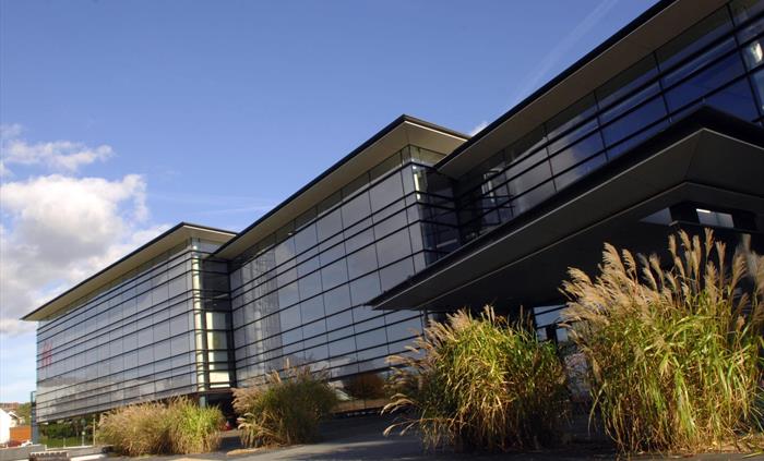a view of the museum from the front, showing the modern part of the building. It is approx 2 stories high, with a flat roof and the sides are all glas